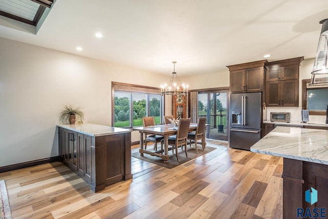 kitchen featuring light stone countertops, high quality fridge, dark brown cabinets, light hardwood / wood-style floors, and kitchen peninsula