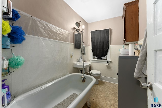 bathroom featuring a tub to relax in, sink, tile walls, and toilet