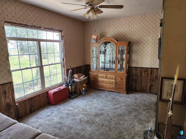 interior space featuring carpet floors, a wealth of natural light, wooden walls, and ceiling fan