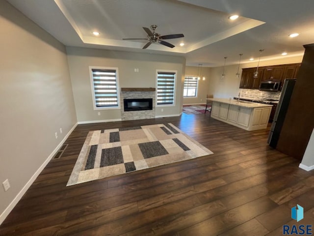 unfurnished living room with ceiling fan, dark hardwood / wood-style flooring, a wealth of natural light, and a tray ceiling