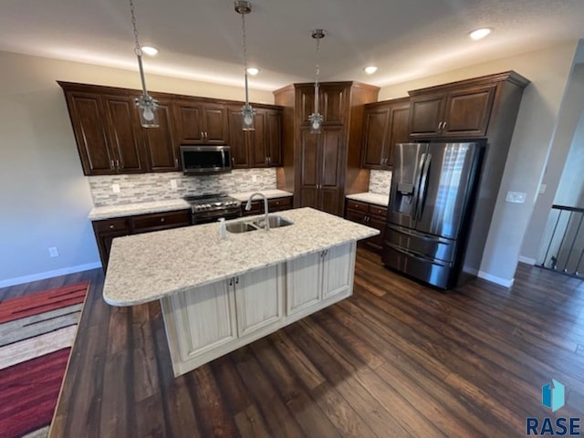 kitchen with a center island with sink, sink, stainless steel appliances, and hanging light fixtures