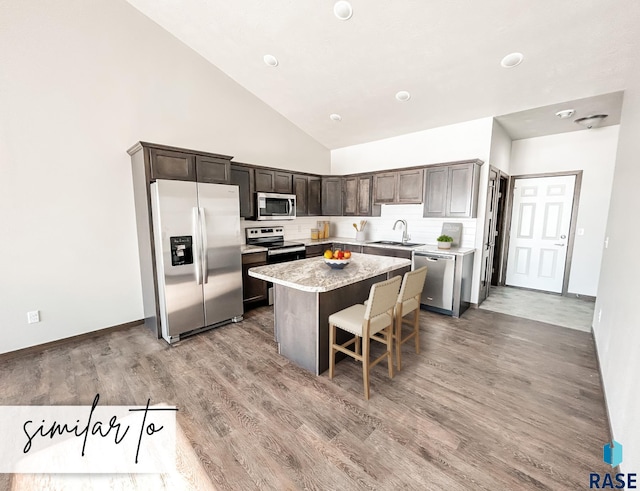 kitchen with dark brown cabinetry, appliances with stainless steel finishes, a breakfast bar, a kitchen island, and light wood-type flooring