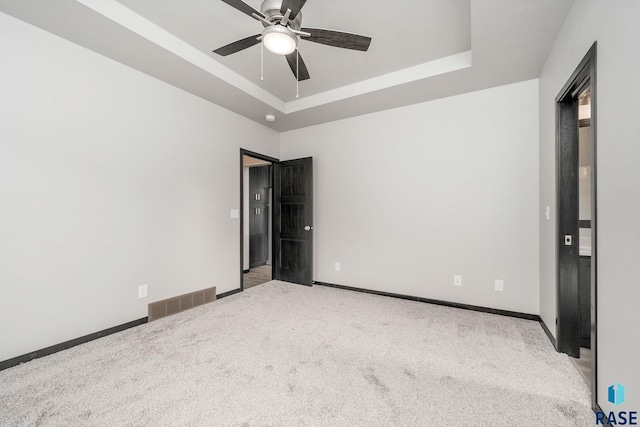 carpeted spare room with ceiling fan and a raised ceiling