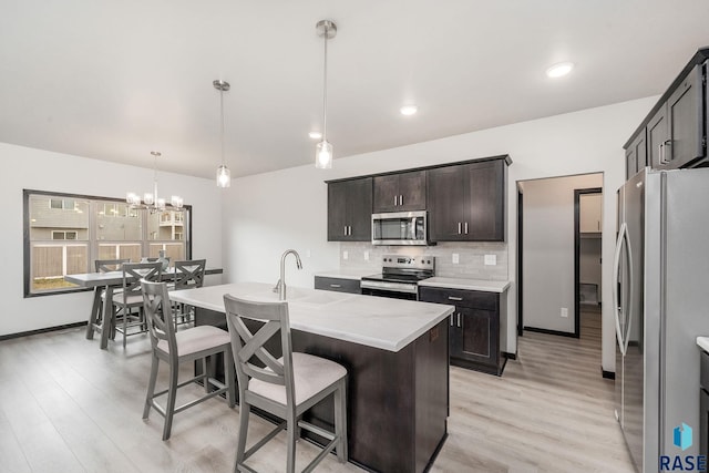 kitchen featuring hanging light fixtures, light hardwood / wood-style flooring, a kitchen island with sink, dark brown cabinets, and appliances with stainless steel finishes