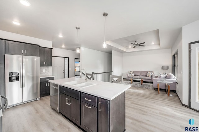 kitchen with light wood-type flooring, stainless steel appliances, ceiling fan, sink, and an island with sink