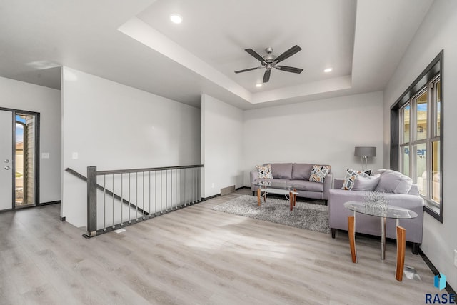 living room featuring light wood-type flooring, a raised ceiling, ceiling fan, and a healthy amount of sunlight