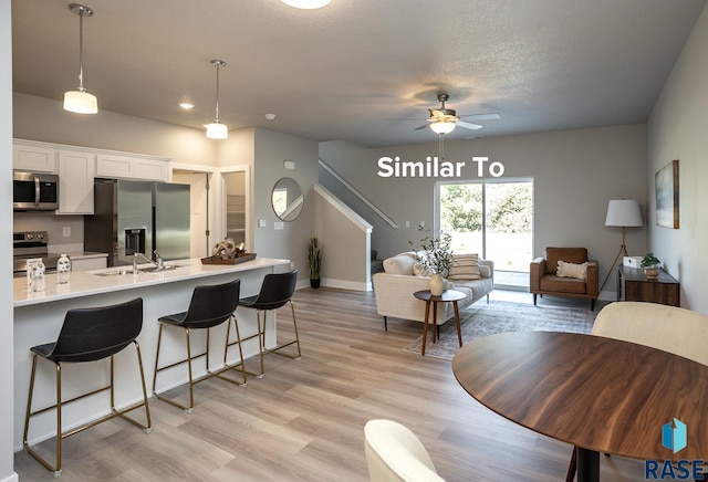 kitchen with pendant lighting, white cabinets, a kitchen bar, stainless steel appliances, and sink