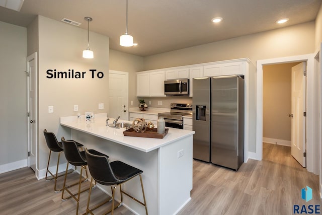 kitchen featuring white cabinets, appliances with stainless steel finishes, decorative light fixtures, kitchen peninsula, and light wood-type flooring