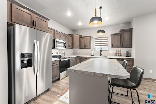 kitchen featuring a kitchen breakfast bar, stainless steel appliances, sink, decorative light fixtures, and a kitchen island