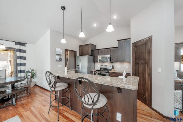 kitchen featuring light hardwood / wood-style flooring, vaulted ceiling, decorative light fixtures, dark brown cabinets, and stainless steel appliances