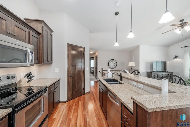 kitchen with a kitchen island with sink, hanging light fixtures, sink, light hardwood / wood-style flooring, and appliances with stainless steel finishes