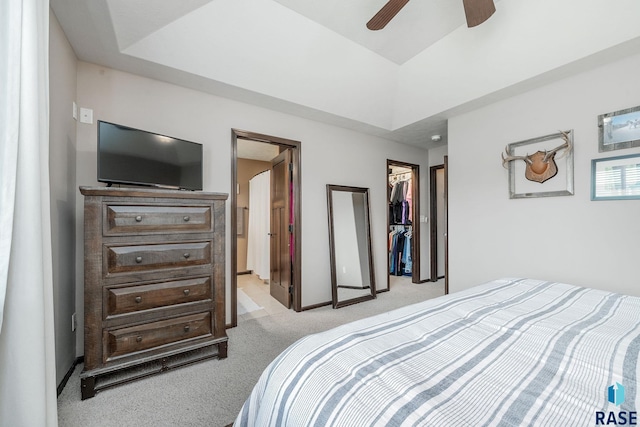 bedroom with a walk in closet, ensuite bath, light colored carpet, ceiling fan, and a closet