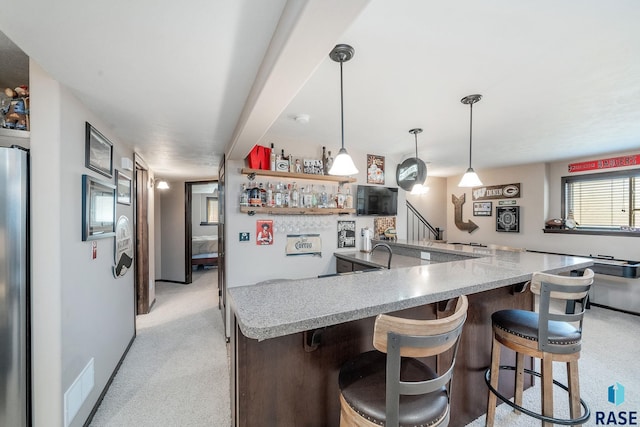 kitchen with a breakfast bar, hanging light fixtures, light stone countertops, kitchen peninsula, and stainless steel refrigerator