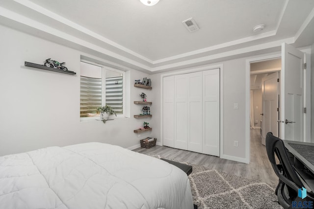 bedroom with a tray ceiling, light hardwood / wood-style flooring, and a closet