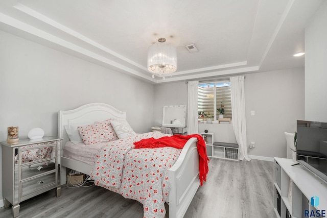 bedroom with wood-type flooring, an inviting chandelier, and a raised ceiling