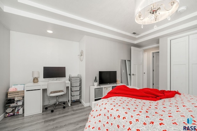 bedroom with a raised ceiling, light wood-type flooring, and a closet