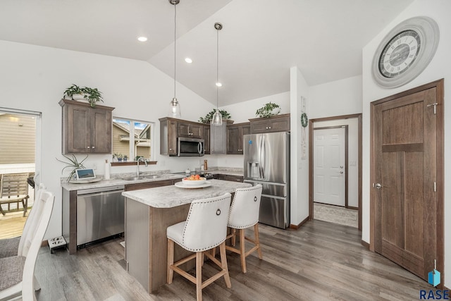 kitchen featuring pendant lighting, lofted ceiling, appliances with stainless steel finishes, a kitchen island, and dark hardwood / wood-style flooring