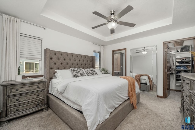 carpeted bedroom featuring ceiling fan, a closet, a walk in closet, and a tray ceiling