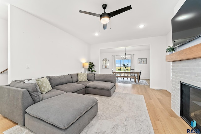 living room featuring light hardwood / wood-style flooring, ceiling fan with notable chandelier, and a brick fireplace