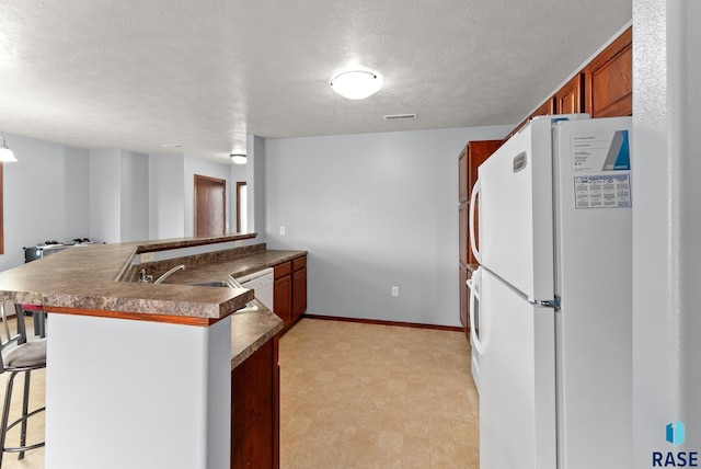 kitchen featuring white appliances, a textured ceiling, decorative light fixtures, a kitchen bar, and kitchen peninsula