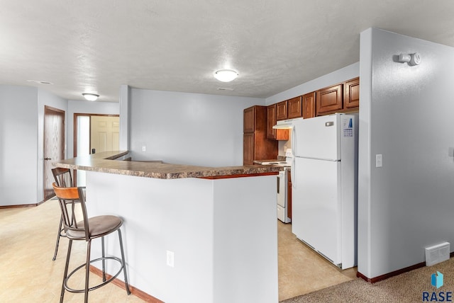 kitchen featuring a breakfast bar area, a textured ceiling, and white appliances