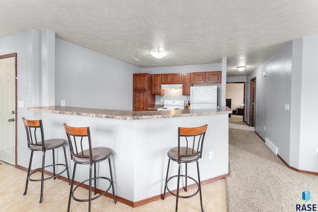 kitchen featuring a kitchen breakfast bar, white appliances, kitchen peninsula, and light carpet