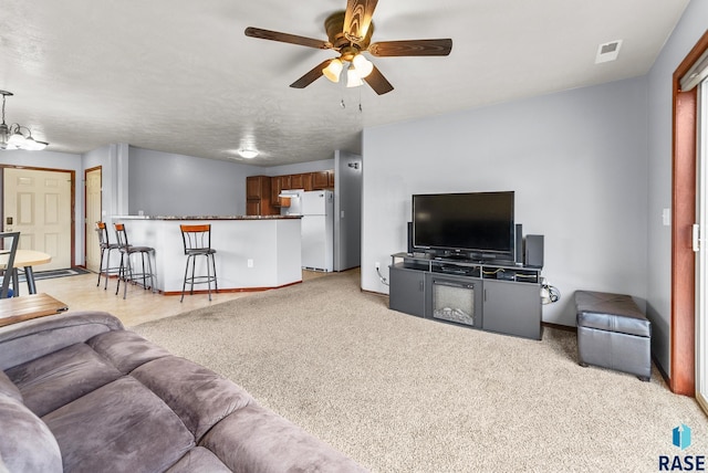 living room with a textured ceiling, light colored carpet, and ceiling fan with notable chandelier