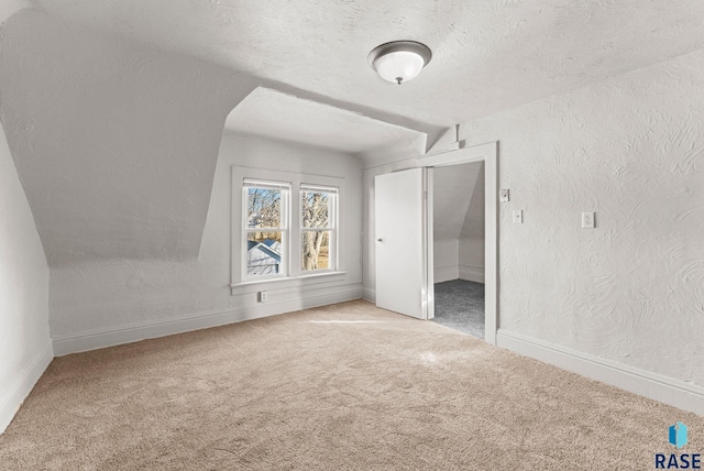 additional living space featuring a textured ceiling, light colored carpet, and lofted ceiling