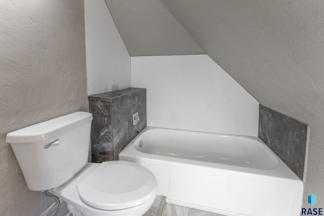 bathroom with a washtub, toilet, and lofted ceiling