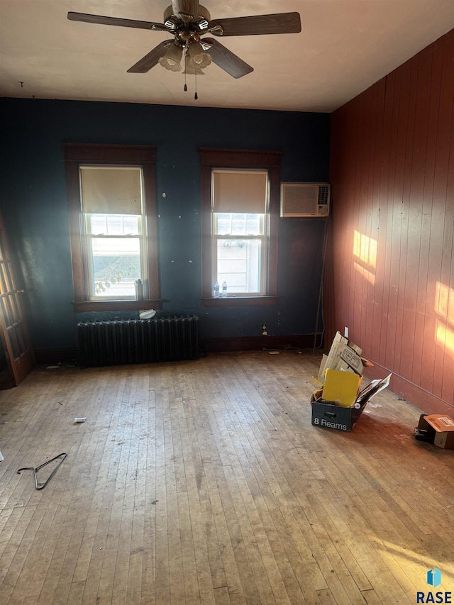 spare room with a wall unit AC, radiator, plenty of natural light, and wood-type flooring