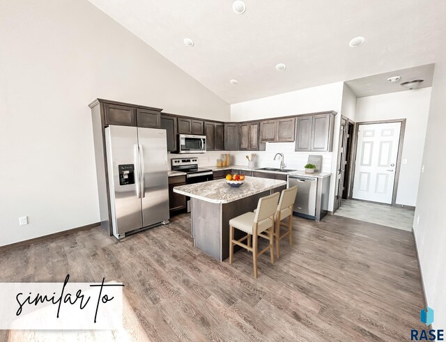 kitchen with a kitchen breakfast bar, dark brown cabinets, stainless steel appliances, light hardwood / wood-style floors, and a kitchen island