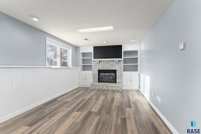 unfurnished living room featuring a textured ceiling, wooden walls, wood-type flooring, built in features, and a fireplace