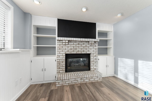 unfurnished living room featuring built in shelves, a fireplace, a textured ceiling, and hardwood / wood-style flooring