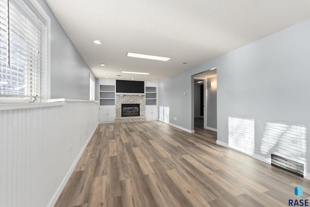 unfurnished living room with built in features, wood-type flooring, a textured ceiling, and a brick fireplace