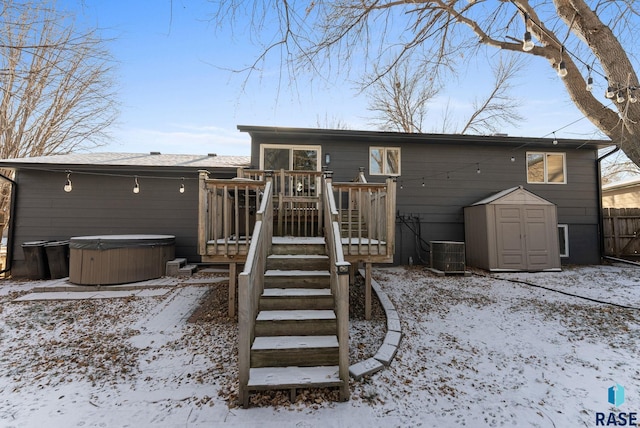 snow covered rear of property with central air condition unit, a wooden deck, a shed, and a hot tub