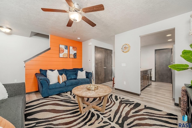 living room with ceiling fan, light wood-type flooring, and a textured ceiling