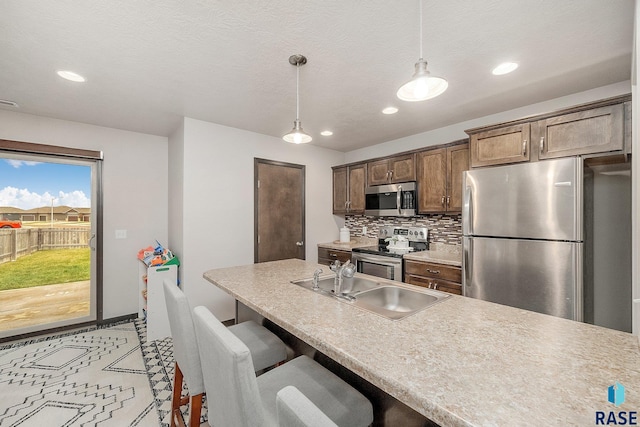 kitchen featuring sink, hanging light fixtures, stainless steel appliances, a kitchen breakfast bar, and decorative backsplash