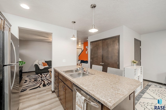 kitchen featuring stainless steel appliances, sink, decorative light fixtures, a center island, and light hardwood / wood-style floors