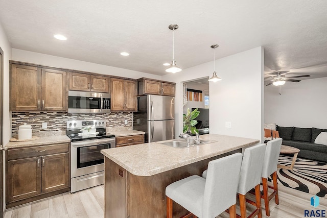 kitchen featuring a kitchen bar, appliances with stainless steel finishes, sink, light hardwood / wood-style flooring, and hanging light fixtures