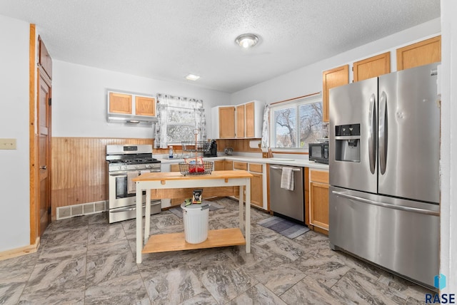 kitchen featuring wood walls, light brown cabinetry, stainless steel appliances, and a textured ceiling