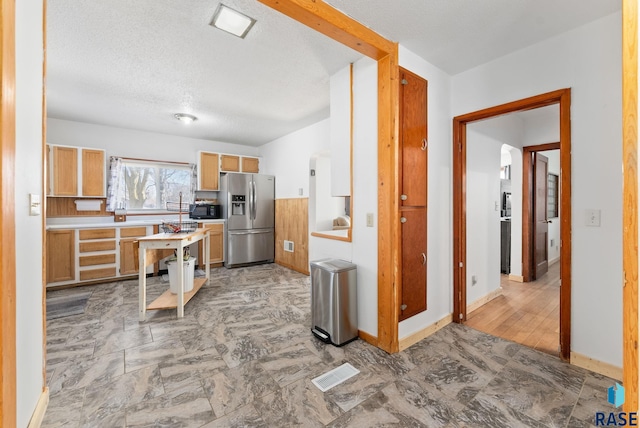 kitchen featuring stainless steel fridge with ice dispenser, light brown cabinetry, and a textured ceiling