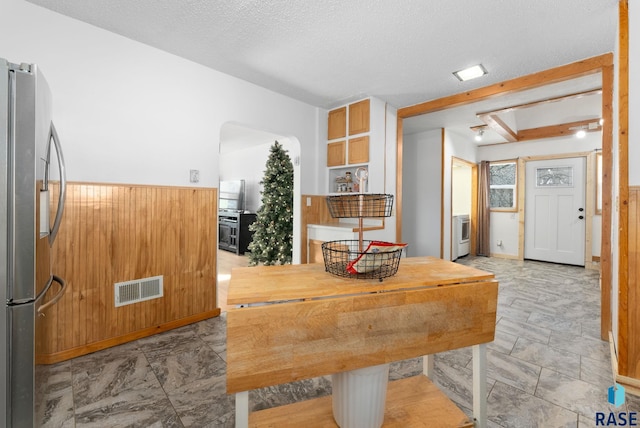 interior space featuring beam ceiling, a textured ceiling, and wood walls