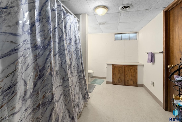 bathroom with a drop ceiling, a shower with shower curtain, and toilet