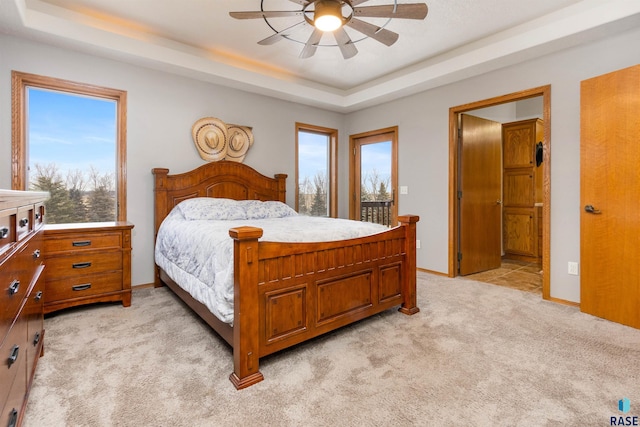 carpeted bedroom featuring a raised ceiling, multiple windows, and ceiling fan