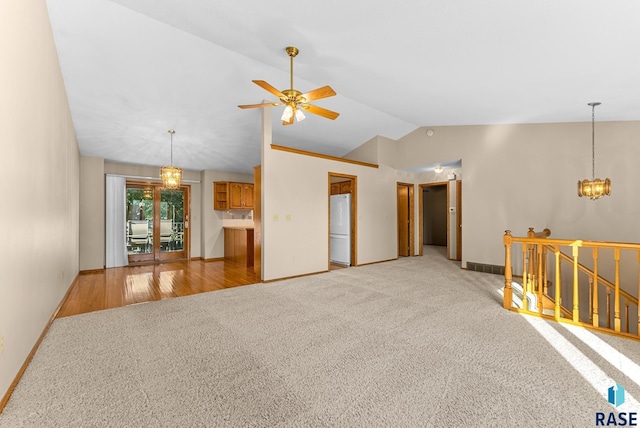 empty room with ceiling fan with notable chandelier, light wood-type flooring, and vaulted ceiling