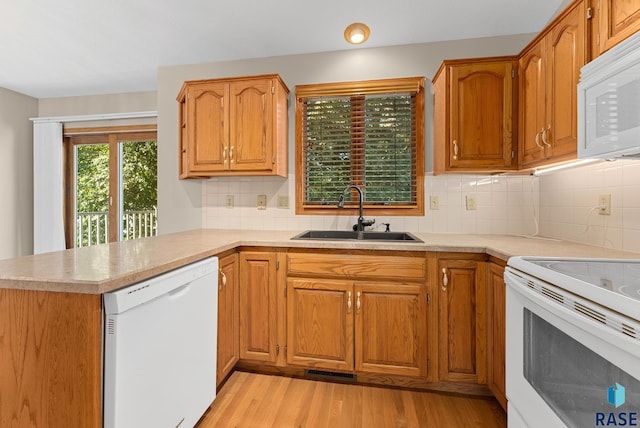 kitchen featuring white appliances, backsplash, sink, light hardwood / wood-style floors, and kitchen peninsula