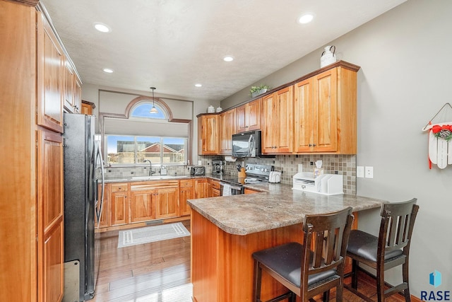 kitchen featuring kitchen peninsula, refrigerator, light hardwood / wood-style floors, hanging light fixtures, and stainless steel range with electric cooktop