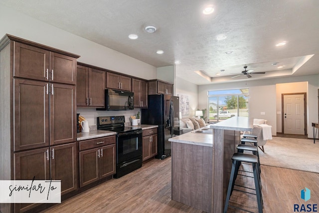 kitchen with dark brown cabinets, black appliances, light hardwood / wood-style floors, a kitchen island, and a breakfast bar area