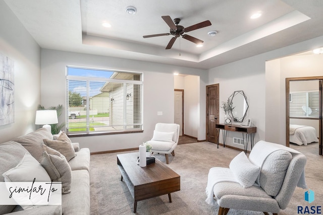 carpeted living room with a tray ceiling and ceiling fan