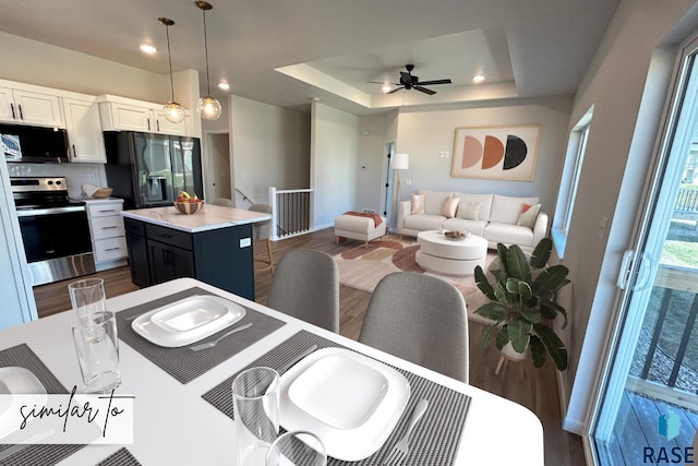 kitchen with a center island, pendant lighting, a tray ceiling, white cabinets, and black appliances